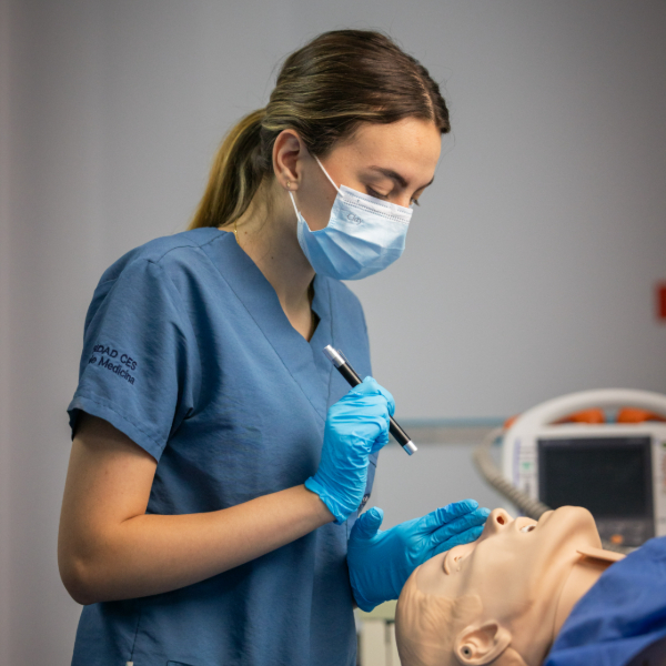 Persona con uniforme clínico y guantes azules realizando un procedimiento en un simulador.