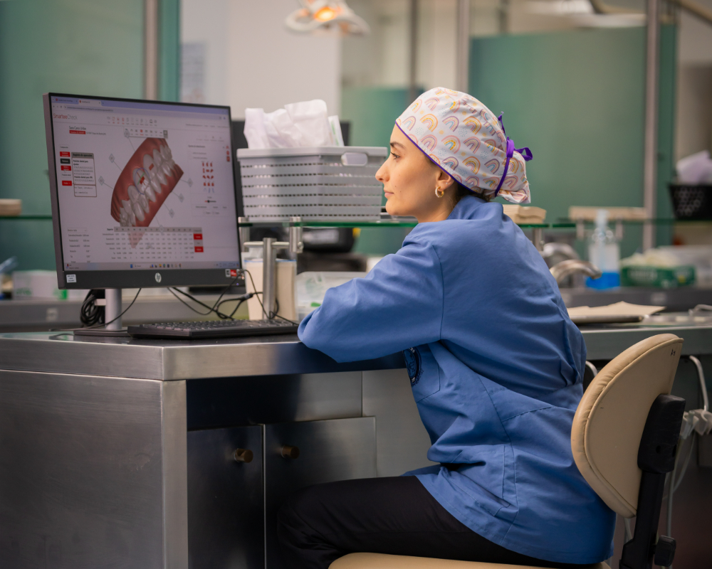 Una persona con uniforme clínico observa en un monitor una imagen digital de dientes, en un entorno de laboratorio o consultorio odontológico.