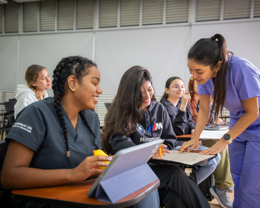 Varias personas en un aula, con una persona de pie explicando algo a otras que están sentadas y tomando notas.
