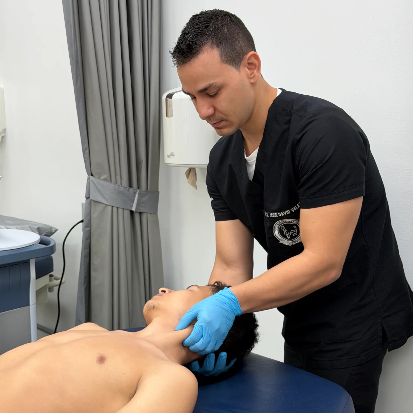 Profesional de la salud aplica una técnica de evaluación o terapia manual en la región cervical de una persona recostada sobre una camilla, utilizando guantes en un entorno clínico de rehabilitación física.