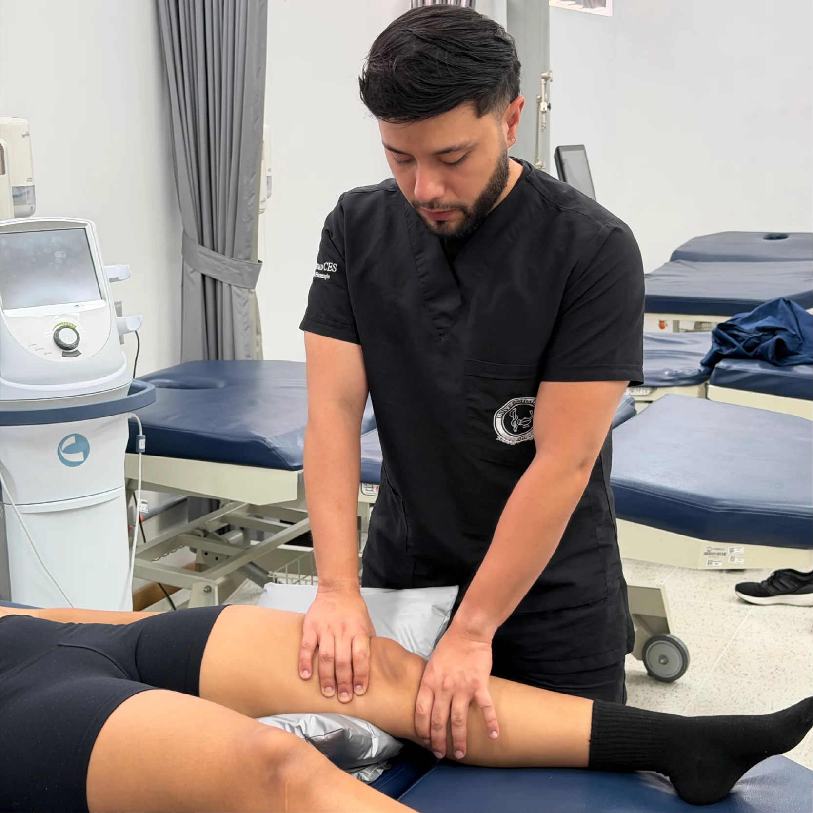 Profesional de la salud aplica una técnica de evaluación o terapia manual sobre la pierna de una persona recostada en una camilla, en un entorno clínico equipado para rehabilitación y atención física.