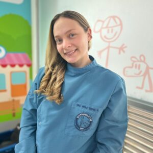 Persona con uniforme clínico azul de pie en un entorno con paredes decoradas con dibujos infantiles
