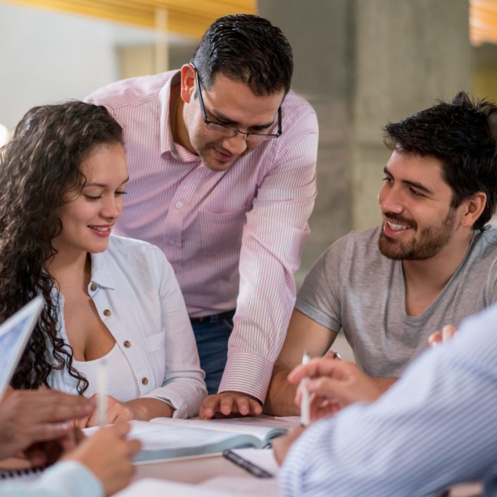 Varias personas están reunidas alrededor de una mesa en un espacio interior, revisando documentos y tomando notas, en lo que parece ser una actividad colaborativa.