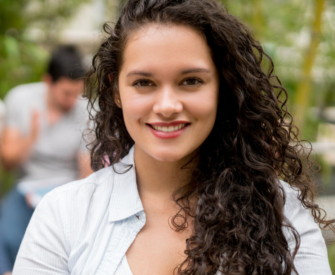 Persona con cabello rizado y largo sostiene un cuaderno abierto en un espacio exterior con vegetación al fondo.