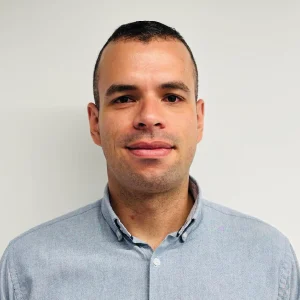 Persona de pie frente a una pared clara, usando camisa de manga larga color gris claro con cuello abotonado.