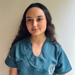 Persona con uniforme clínico verde, que muestra el logotipo institucional en el pecho, de pie frente a un fondo claro.