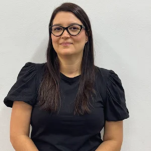 Persona con cabello largo y liso, vestida con camiseta negra de mangas abullonadas, sentada frente a un fondo blanco liso.