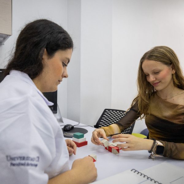 Dos personas en un consultorio realizando una actividad con bloques sobre un escritorio.