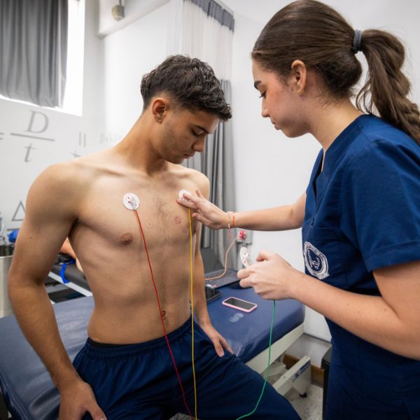 Una persona con uniforme clínico coloca electrodos en el pecho de otra persona para realizar una práctica de electrocardiografía en un entorno de salud.