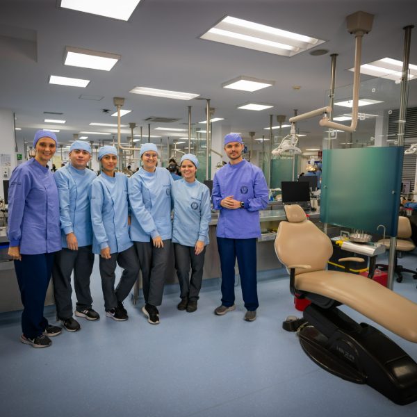 Grupo de personas con uniforme clínico azul está de pie en un consultorio odontológico equipado, junto a una silla dental.