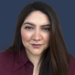 La imagen muestra a una persona de frente, con el cabello largo, liso y castaño oscuro, peinado hacia ambos lados. Viste una blusa de color vinotinto con cuello tipo camisa. El fondo es liso y de color azul oscuro, con iluminación uniforme y sin elementos adicionales.