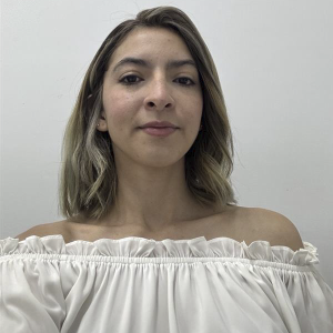 Persona de pie vistiendo una blusa blanca de hombros descubiertos con volantes, frente a un fondo liso de color claro.