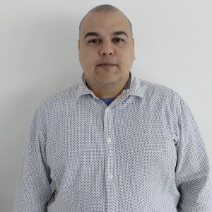 Persona de pie vistiendo una camisa de botones con estampado pequeño en tonos blanco y azul, frente a un fondo liso claro.