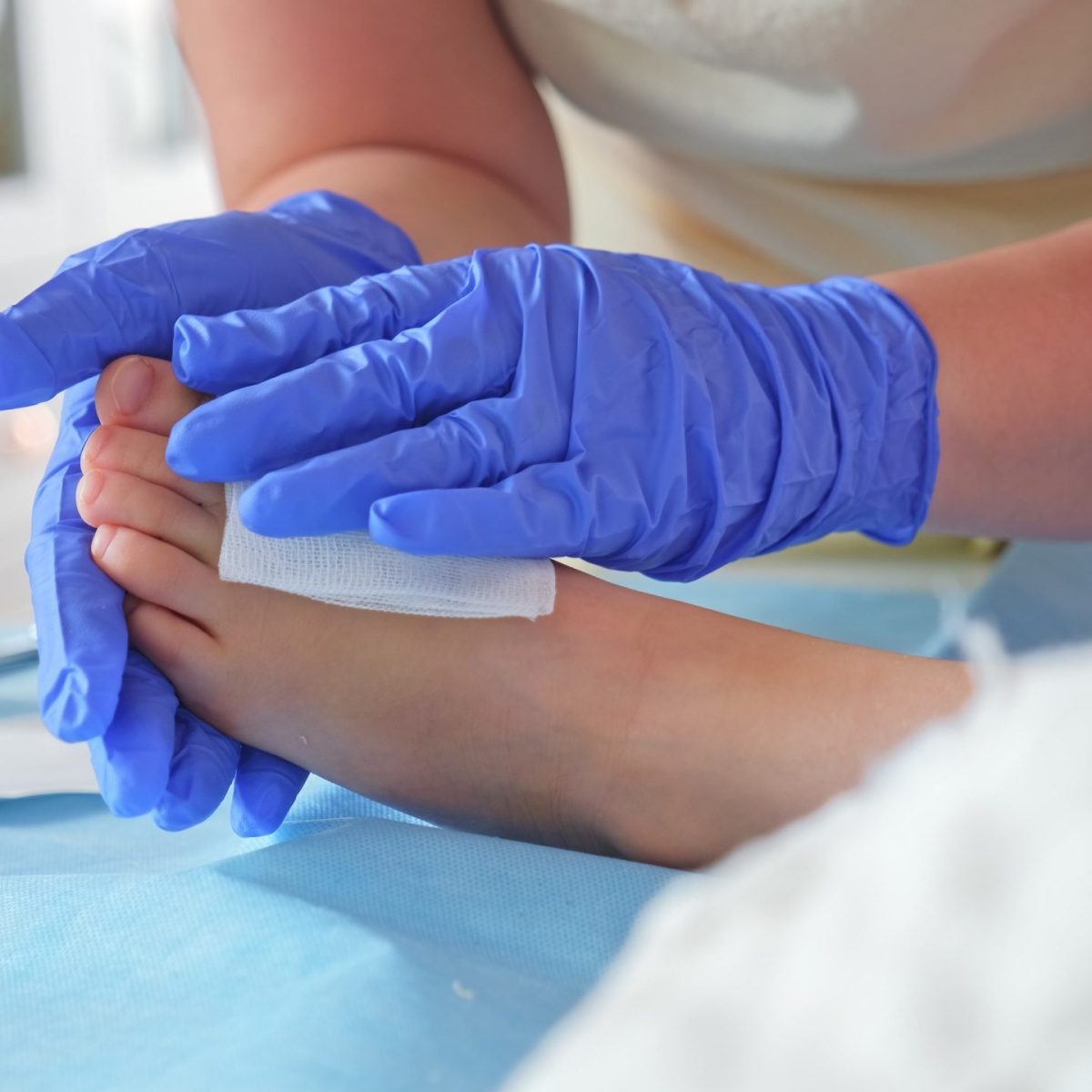Manos con guantes médicos curan el pie de una persona utilizando una gasa.