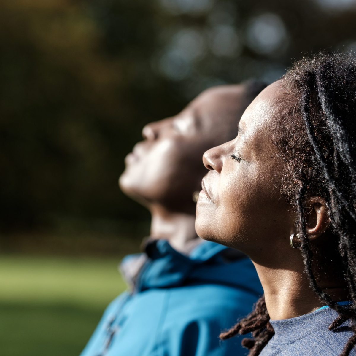 Dos personas están al aire libre mirando hacia arriba, con un fondo de áreas verdes y árboles.
