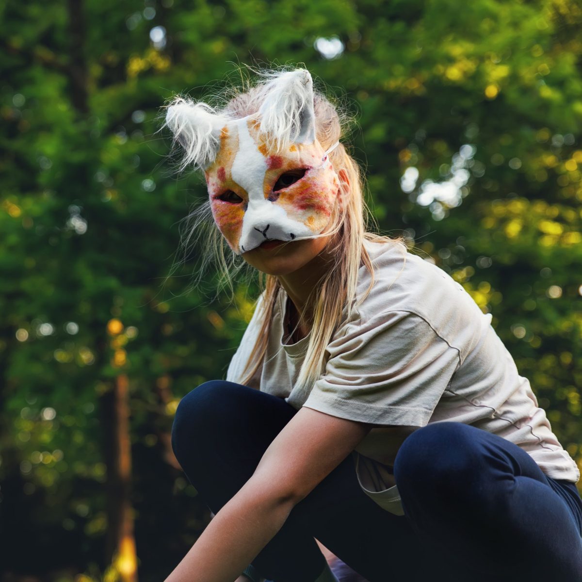 Persona agachada en un entorno natural, con disfraz de zorro y árboles verdes en el fondo.