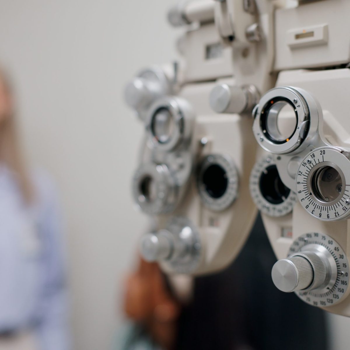 Equipo de optometría utilizado para evaluar la visión en un consultorio, con una persona de pie al fondo.