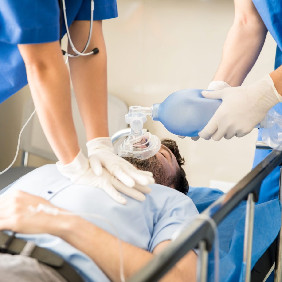 Personal de salud realiza maniobras de reanimación a una persona acostada en una camilla, aplicando compresiones torácicas y ventilación con mascarilla.