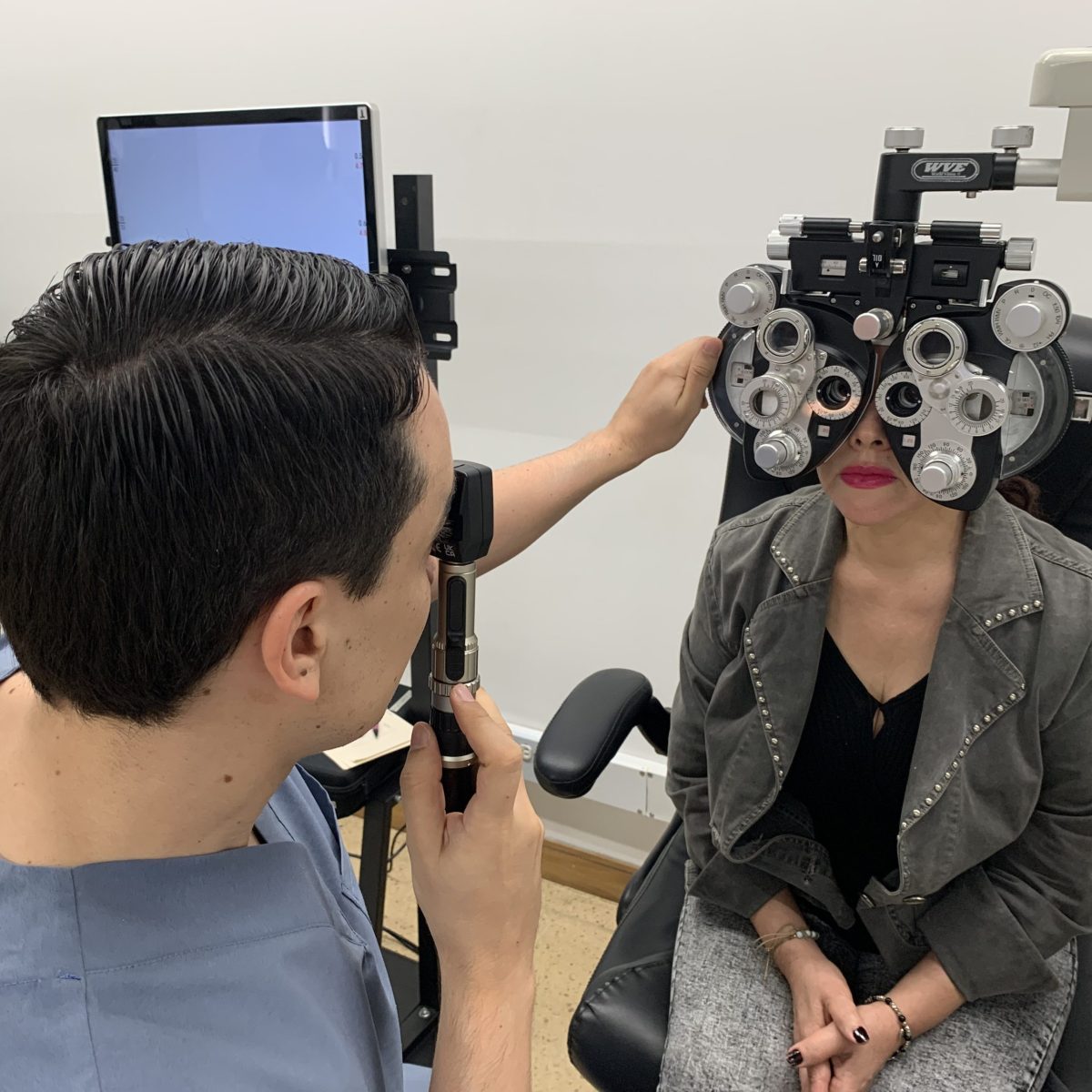 Un profesional de la salud visual realiza un examen de refracción utilizando un foróptero mientras la persona examinada está sentada frente al equipo.