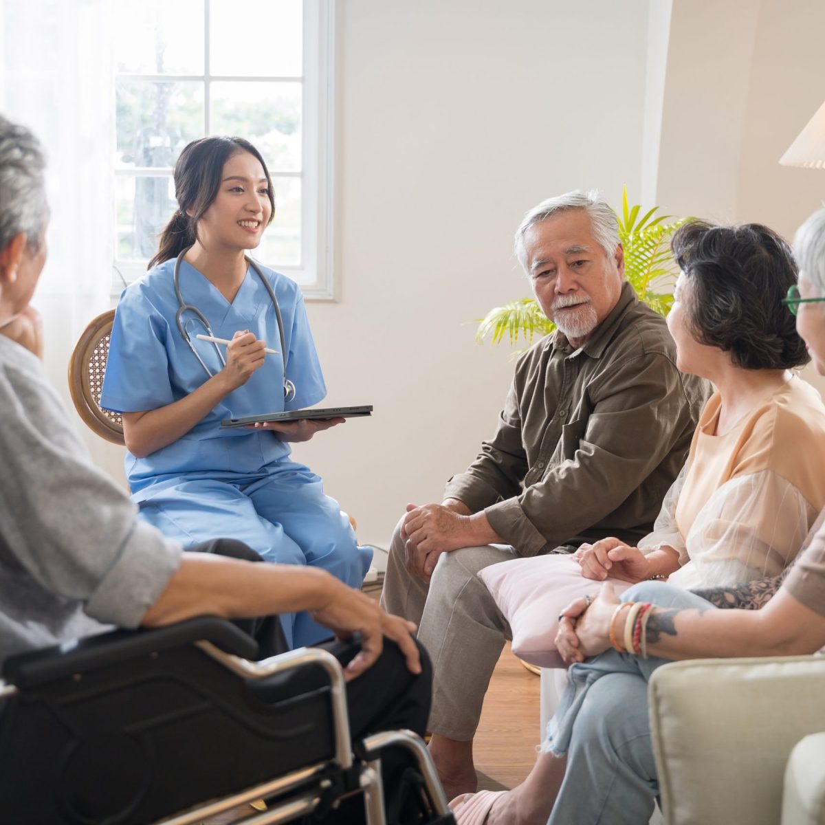 Grupo de personas adultas mayores sentadas en círculo en una sala iluminada, junto a una persona con uniforme médico.