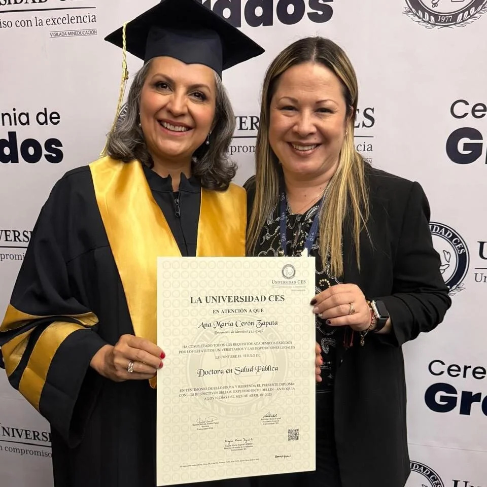 Fotografía de dos personas de pie frente a un fondo institucional de la Universidad CES. Una de ellas viste toga y birrete y ambas sostienen un diploma donde se lee “La Universidad CES” y el título “Doctora en Salud Pública”, con el nombre “Ana María Cerón Zapata”. El fondo incluye logotipos y texto de ceremonia de grados.