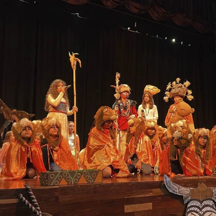 Grupo de niños en un escenario, vistiendo vestuarios temáticos y accesorios, durante una presentación teatral.