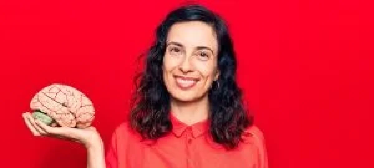 Persona vestida con camisa roja sostiene un modelo anatómico de un cerebro en una mano, sobre fondo rojo.
