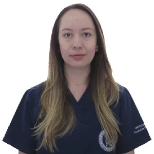 Persona de pie frente a un fondo blanco, vistiendo uniforme médico azul oscuro con escudo visible en la parte superior.