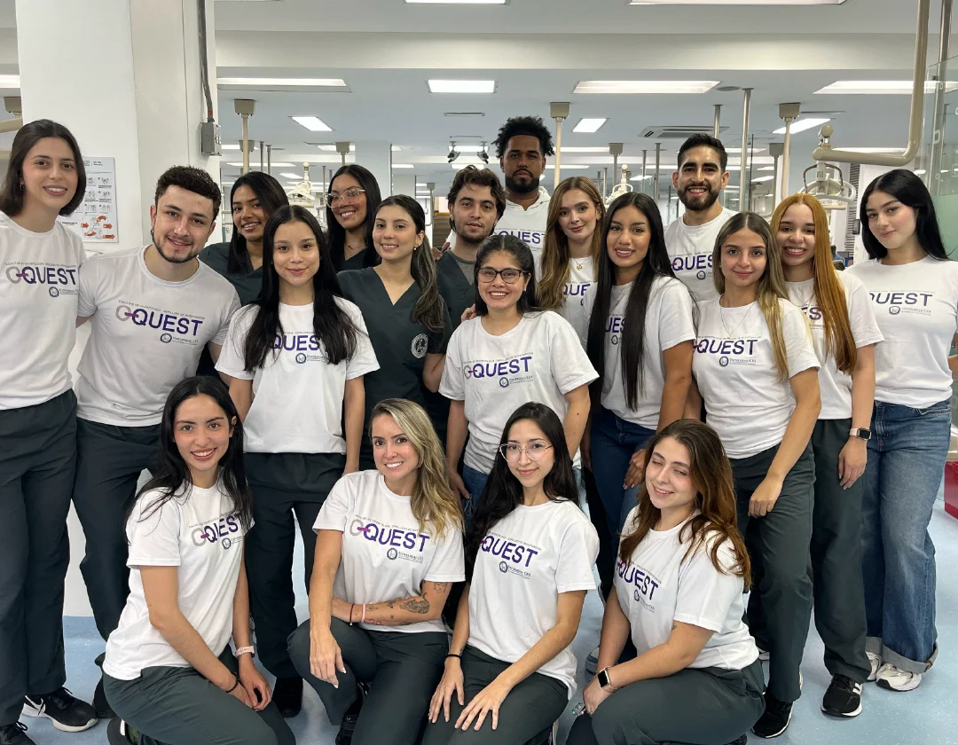 Grupo de personas en un laboratorio, posando juntas y vistiendo camisetas blancas con texto visible, en un entorno interior con equipos clínicos.