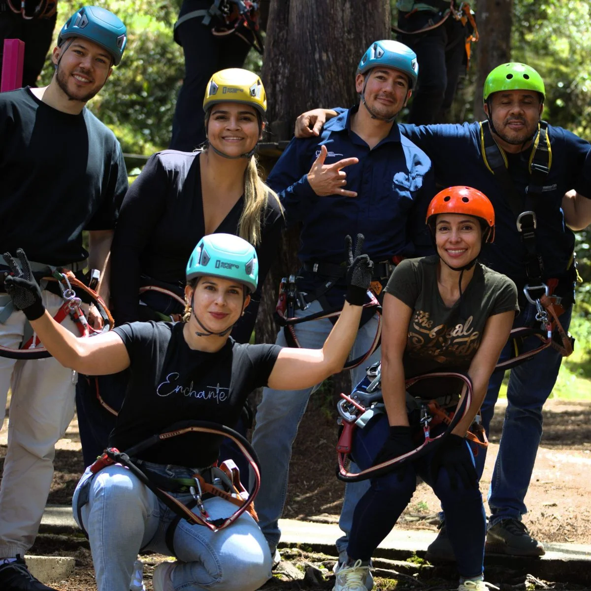 Grupo de personas con cascos y arneses de seguridad posan juntas en un entorno natural con árboles, durante una actividad de aventura al aire libre.