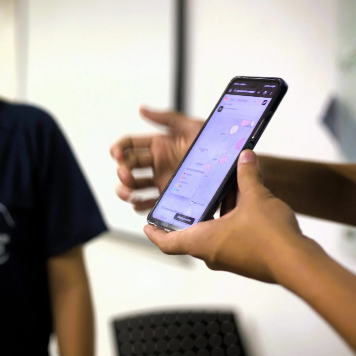 Manos sostienen un teléfono inteligente mientras una de ellas interactúa con la pantalla, que muestra una aplicación con gráficos.