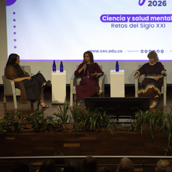 Tres personas sentadas en un escenario participan en un panel académico, con micrófonos y botellas de agua, frente a una pantalla con texto sobre ciencia y salud mental.