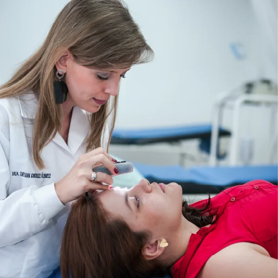 Profesional de la salud examina la piel de una persona recostada utilizando un dispositivo manual en un entorno clínico.