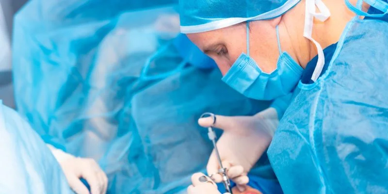 Profesional de salud con equipo quirúrgico realiza un procedimiento dental utilizando instrumentos dentro de la boca de un paciente, en un entorno clínico.