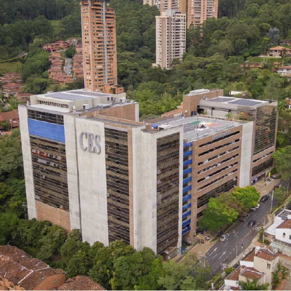 Edificio institucional de gran altura con el nombre ‘CES’ en la fachada, rodeado de vegetación y vías urbanas, en un entorno montañoso con otras edificaciones residenciales.