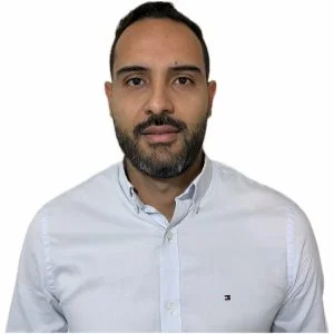 Persona de pie frente a un fondo liso claro, vistiendo una camisa blanca de botones con cuello abotonado.
