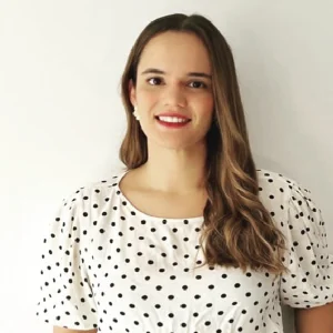 Persona de pie frente a un fondo liso claro, vistiendo una blusa blanca con estampado de puntos negros y mangas cortas abullonadas.