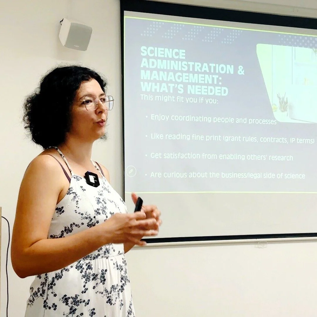 Persona realizando una presentación en un aula frente a una pantalla de proyección. La diapositiva muestra información sobre “Science Administration & Management” y las habilidades e intereses relacionados con esta área profesional.