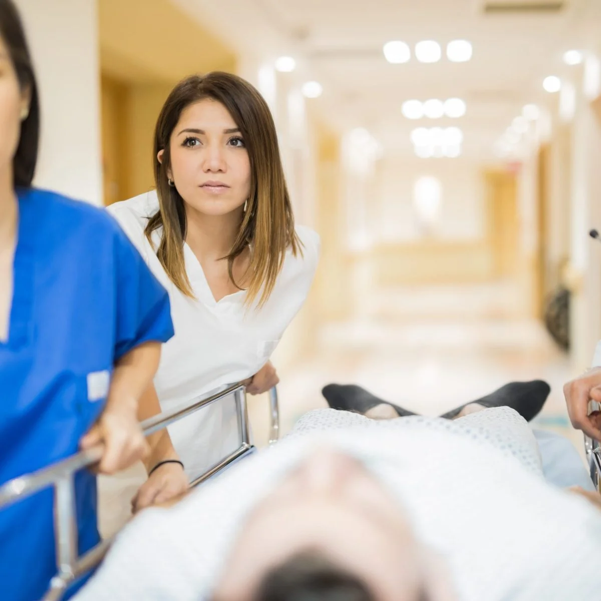 Personal de atención en salud traslada a un paciente en una camilla por un pasillo hospitalario. Varias personas acompañan el desplazamiento en un entorno clínico iluminado.