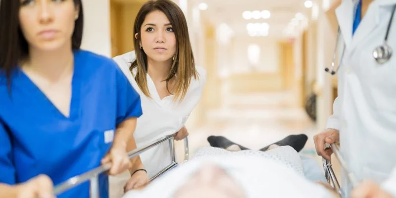 Personal de atención en salud traslada a un paciente en una camilla por un pasillo hospitalario. Varias personas acompañan el desplazamiento en un entorno clínico iluminado.