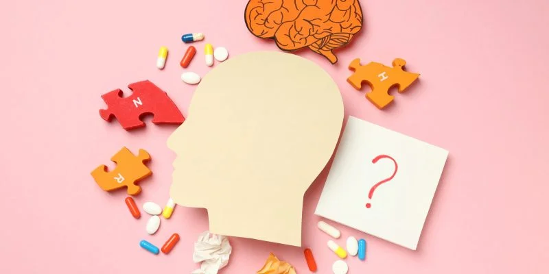 Ilustración conceptual sobre salud cerebral y trastornos neurológicos. Se observa la silueta de una cabeza humana rodeada por piezas de rompecabezas, cápsulas y tabletas, un dibujo de un cerebro y una nota con un signo de interrogación sobre un fondo rosa.