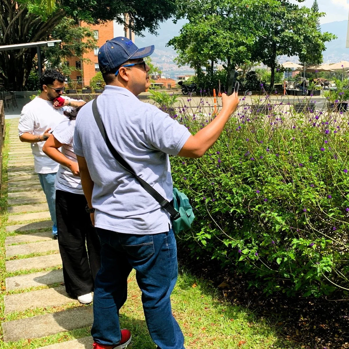 Grupo de personas participa en una actividad de observación en un jardín, registrando información sobre plantas con flores moradas junto a un sendero al aire libre.