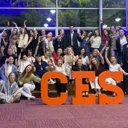 Fotografía grupal de participantes en un encuentro institucional de la Universidad CES. Las personas posan frente a unas letras de gran formato con la sigla “CES”, en un espacio interior.