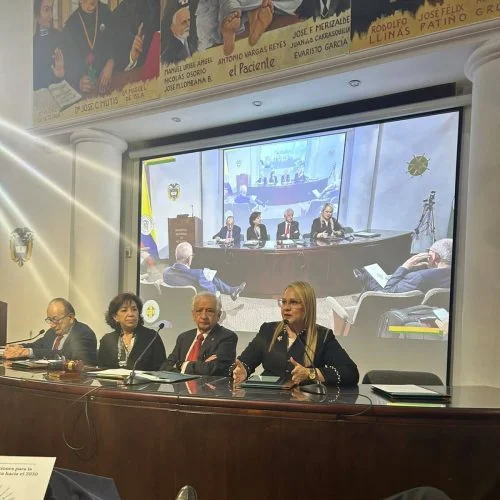 Panel académico realizado en un auditorio institucional. Varias personas participan en una mesa de discusión frente al público, mientras una pantalla proyecta una transmisión o presentación relacionada con temas de salud, educación o investigación.