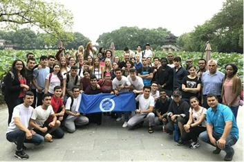Grupo numeroso de personas reunidas al aire libre, posando para una foto con una bandera azul con el logo del CES; detrás se observa vegetación y estructuras en un entorno tipo parque.