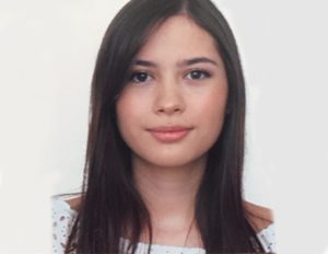 Persona con cabello largo y liso, vestida con una blusa blanca con estampado de puntos y hombros descubiertos, frente a un fondo blanco uniforme.