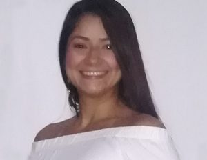 Persona con cabello largo y liso, vestida con una blusa blanca de hombros descubiertos, frente a un fondo liso de color claro.