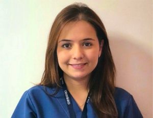 Persona con uniforme clínico azul y gafete colgado al cuello, frente a un fondo claro.