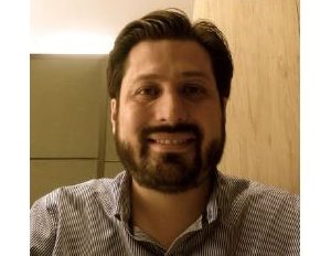 Persona con camisa de rayas verticales en tonos claros y oscuros, sentada frente a una pared de madera clara y otra pared en tono beige.