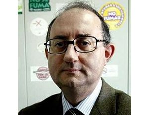 Persona con traje formal y corbata está frente a un fondo con varios adhesivos que incluyen mensajes como “No fumar”.